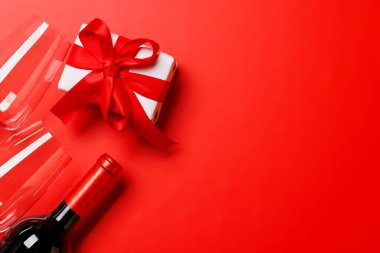 Bir kadeh ve bir şişe kırmızı şarap zarif bir sevgililer günü hediye kutusuyla, canlı kırmızı bir arka planda ayarlanmış, romantik ve lüks bir atmosfer yaratıyor.
