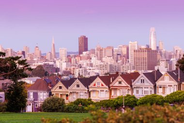 San Francisco 'daki Boyalı Kadınlar' ın canlı günbatımı manzarası. Renkli gökyüzünün ılık renkleri altında parlayan ikonik Viktorya dönemi evleri. Arka planda gökyüzü var.
