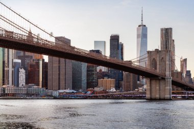 Manhattan 'a doğru uzanan Brooklyn Köprüsü' nün panoramik günbatımı manzarası, solan gökyüzüne karşı sıcak renklerle aydınlatılan gökdelenler.