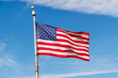 Güneşli mavi gökyüzüne karşı dalgalanan Amerikan bayrağı, canlı renklerle vatansever gururunu sergiliyor.