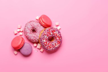 Renkli badem kurabiyeleri ve pastel pembe arka planda donutlardan oluşan göz alıcı bir düzenleme. Gösterişli tatlılar ya da eğlenceli ve hareketli estetik tatlılar için mükemmel.