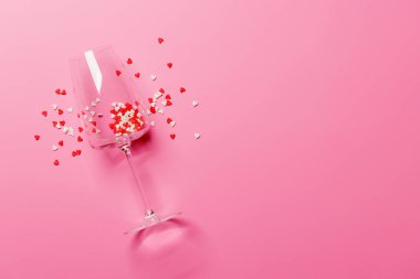 Kalp şeklinde bir dekorla süslenmiş canlı pembe bir arka planda, Sevgililer Günü için aşkı ve kutlamayı simgeleyen bir şampanya kadehi.