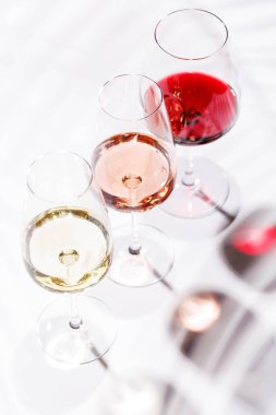 Kırmızı, beyaz ve gül şarabıyla dolu üç şarap kadehi parlak, minimalist arka planda zarif bir şekilde duruyor. Şarabın çeşitliliğinin ve zarafetinin canlı bir gösterisi.