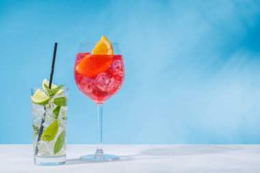 Masada açık mavi bir arkaplan üzerine çeşitli kokteyller serpiştirilmiş, güneşli parıltılar ve neşeli gölgelerle güçlendirilmiş.