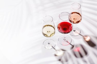 Kırmızı, beyaz ve gül şarabıyla dolu üç şarap kadehi parlak, minimalist arka planda zarif bir şekilde duruyor. Şarabın çeşitliliğinin ve zarafetinin canlı bir gösterisi.