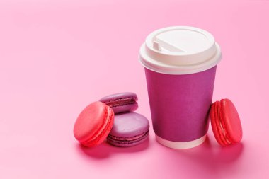 Renkli badem kurabiyelerinden oluşan canlı bir düzenleme. Pastel pembe arka planda kağıttan bir kahve fincanıyla eşleştirilmiş. Kahve molası, tatlı ya da kutlama teması için mükemmel.