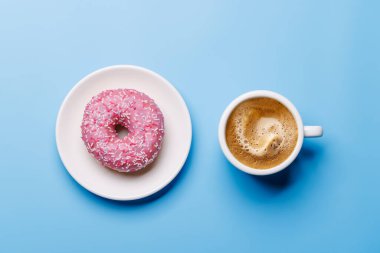 Canlı bir çörek, renkli malzemeler ve mavi arka planda düzenlenmiş bir kahve fincanı düz bir şekilde, neşeli ve iştah açıcı bir sahne yaratıyor.