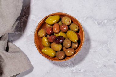 Bir kâse ve zeytin yağı şişesinde sunulan çeşitli zeytinlerin değişik renkleri, dokuları ve tatları sergilenmektedir.