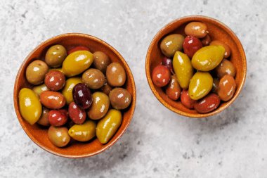 Bir kâse ve zeytin yağı şişesinde sunulan çeşitli zeytinlerin değişik renkleri, dokuları ve tatları sergilenmektedir.