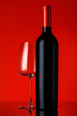 Kırmızı bir şarap şişesi, bir kadeh şarap ve tirbuşon canlı kırmızı bir arka plana yerleştirilip, cesur ve zarif bir kompozisyon oluşturuyor.
