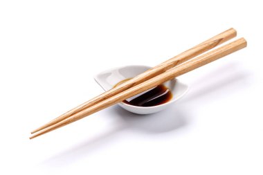 Ahşap yemek çubukları, geleneksel Asya yemeklerini temsil eden temiz beyaz bir zemin üzerinde küçük bir kase soya sosunun yanına nazikçe yerleştirilmiş.