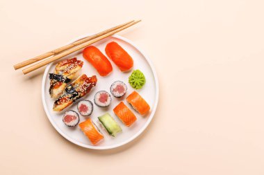 Çeşit çeşit suşi ve maki börekleri, taze malzemeler ve canlı renkler içeren tabakta güzelce düzenlenmiş, bej arkaplanda düz bir zemin üzerinde yatıyordu.