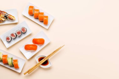 Çeşit çeşit suşi ve maki börekleri, taze malzemeler ve canlı renkler içeren tabaklar üzerinde güzelce düzenlenmiş, bej arkaplanda düz bir şekilde yatıyordu.