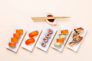 Çeşit çeşit suşi ve maki börekleri, taze malzemeler ve canlı renkler içeren tabaklar üzerinde güzelce düzenlenmiş, bej arkaplanda düz bir şekilde yatıyordu.