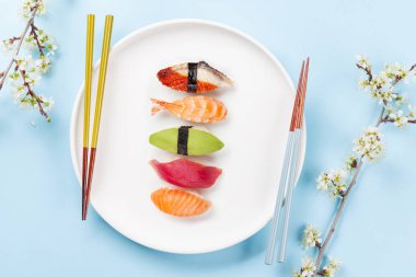 Masadaki suşi tabağı kiraz çiçeği dalıyla süslenmiş ve yemek çubukları Japon yemek kültürünün simgesi.