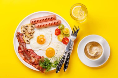Günün başlangıcında sıcak bir fincan kahveyle sunulan, güneşli, kızarmış pastırmalı, sosisli ve taze domatesli klasik bir kahvaltı tabağı.