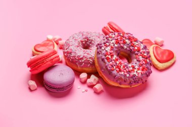 Renkli badem kurabiyeleri ve pastel pembe arka planda donutlardan oluşan göz alıcı bir düzenleme. Gösterişli tatlılar ya da eğlenceli ve hareketli estetik tatlılar için mükemmel.