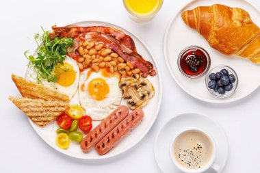 Günün başlangıcında sıcak bir fincan kahveyle sunulan, güneşli, kızarmış pastırmalı, sosisli ve taze domatesli klasik bir kahvaltı tabağı.