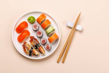 Çeşit çeşit suşi ve maki börekleri, taze malzemeler ve canlı renkler içeren tabakta güzelce düzenlenmiş, bej arkaplanda düz bir zemin üzerinde yatıyordu.