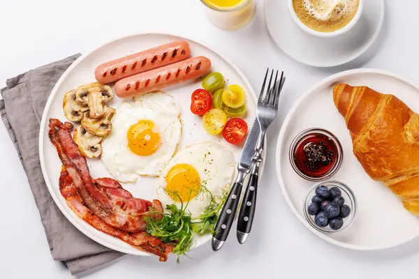 Günün başlangıcında sıcak bir fincan kahveyle sunulan, güneşli, kızarmış pastırmalı, sosisli ve taze domatesli klasik bir kahvaltı tabağı.