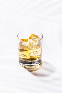 Buzların üzerinde rafine edilmiş bir bardak viski. Kehribar rengi, buz küpleri yavaşça erirken parlıyor. Temiz ve zarif bir sunum için parlak beyaz bir arkaplana kuruluyor.