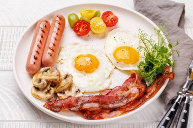 Güne güneşli bir başlangıç için klasik bir kahvaltı tabağı. Yumurtalar, kıtır pastırma, sosis ve taze domatesler.
