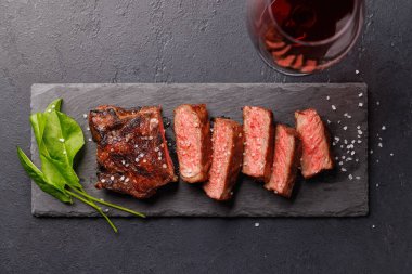 Mükemmel pişirilmiş çizgili biftek sulu, yumuşak bir dokuya sahip koyu arkaplanda kırmızı şarapla eşleştirilmiş. Biftek ve şarap aşıkları için gurme yemeği