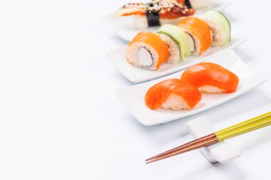 Çeşitli suşi ve maki börekleri, taze malzemeler ve canlı renkler içeren, temiz beyaz arka planda fotokopi alanı olan tabaklar üzerinde güzelce düzenlenmiştir.