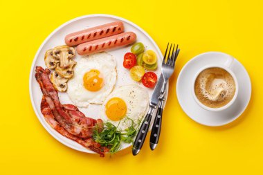 Günün başlangıcında sıcak bir fincan kahveyle sunulan, güneşli, kızarmış pastırmalı, sosisli ve taze domatesli klasik bir kahvaltı tabağı.