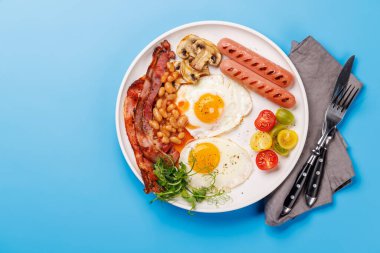 Güne güneşli bir başlangıç için klasik bir kahvaltı tabağı. Yumurtalar, kıtır pastırma, sosis ve taze domatesler.