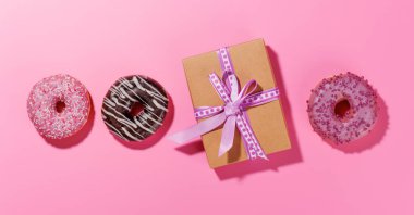 Renkli malzemelerle dolu canlı çörekler ve pembe bir arka planda hediye kutusu olan bir apartman dairesi. Sevgililer Günü kutlamaları için mükemmel.