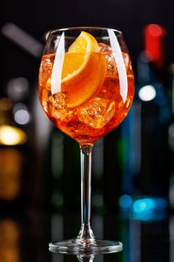 Bar masasında Aperol sprey kokteyli. Arka planda yanan şişelerin renkli bokeh 'i, dinamik ve canlı bir ortam yaratarak ortamı canlandırıyor.