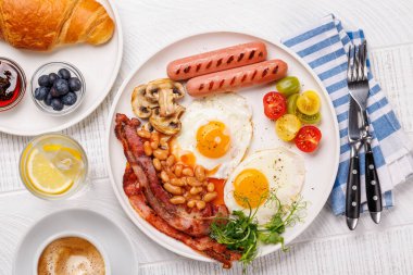 Günün başlangıcında sıcak bir fincan kahveyle sunulan, güneşli, kızarmış pastırmalı, sosisli ve taze domatesli klasik bir kahvaltı tabağı.