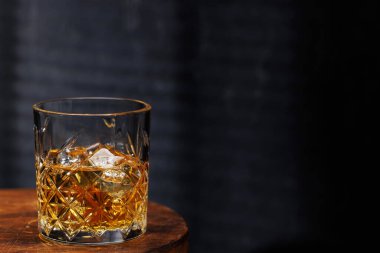 Koyu bir zemine dayanmış, ahşap bir masada dinlenen bir viski bardağı sıcak ve kırsal bir atmosferi çağrıştırıyor.