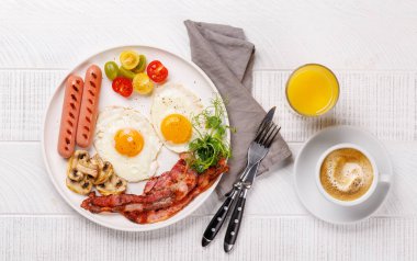 Günün başlangıcında sıcak bir fincan kahveyle sunulan, güneşli, kızarmış pastırmalı, sosisli ve taze domatesli klasik bir kahvaltı tabağı.