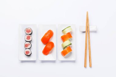 Çeşitli suşi ve maki börekleri, temiz beyaz arka planda taze malzemeler ve canlı renkler içeren tabaklar üzerinde güzelce düzenlenmiş.