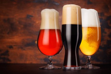 Farklı tipte biralarla dolu çeşitli bira bardakları. Kırsal bir ahşap masada koyu bir arka plana karşı zarif bir şekilde yerleştirilmiş.