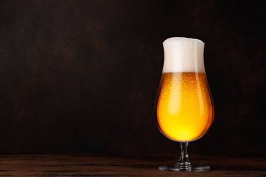 Tahta bir masanın üzerinde altın renkli ve köpüklü bir bardak bira. Bira, bar ve içecek sunumları için ferahlatıcı bir konsept