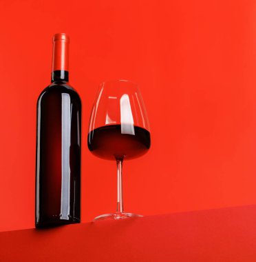 Kırmızı şarap zarafeti: canlı kırmızı arka plana karşı şarap kadehi ve şişe. Kopyalama alanı ile