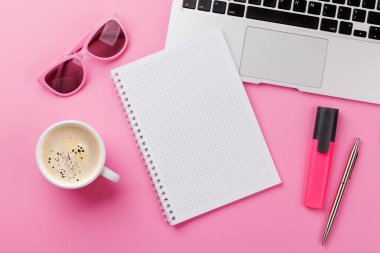 Ofis malzemeleri, kahve fincanı ve boş not defteri olan pembe bir masa. Kopyalama alanı olan kadınsı ve yaratıcı çalışma alanı