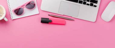 Ofis malzemeleri, kahve fincanı ve dizüstü bilgisayarı olan pembe bir masa. Kopyalama alanı olan kadınsı ve yaratıcı çalışma alanı