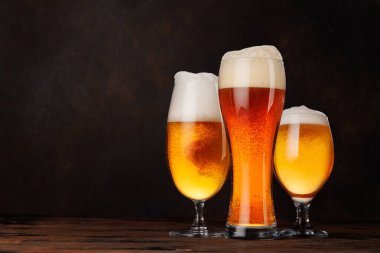 Farklı tipte biralarla dolu çeşitli bira bardakları. Kırsal bir ahşap masada koyu bir arka plana karşı zarif bir şekilde yerleştirilmiş.