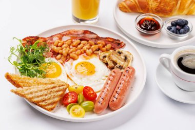 Günün başlangıcında sıcak bir fincan kahveyle sunulan, güneşli, kızarmış pastırmalı, sosisli ve taze domatesli klasik bir kahvaltı tabağı.
