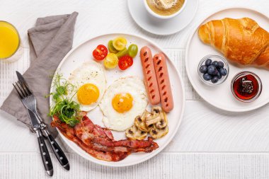 Günün başlangıcında sıcak bir fincan kahveyle sunulan, güneşli, kızarmış pastırmalı, sosisli ve taze domatesli klasik bir kahvaltı tabağı.