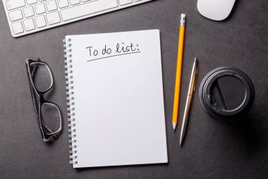 Bilgisayarlı düzenli çalışma masası, ofis malzemeleri, kahve ve yapılacaklar listesi için bir not defteri. Temiz, üretken planlı üst görünüm