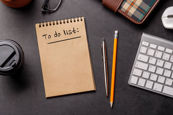 Organized work desk setup with PC, office supplies, coffee and a notepad for writing a to-do list. Top view with clean, productive layout