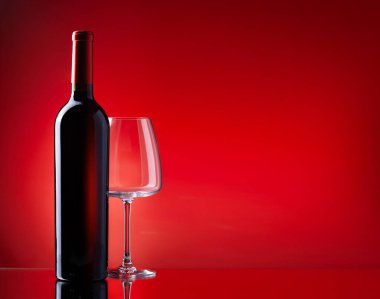 Kırmızı şarap kadehi ve kırmızı zemin üzerinde fotokopi alanı olan şişe.