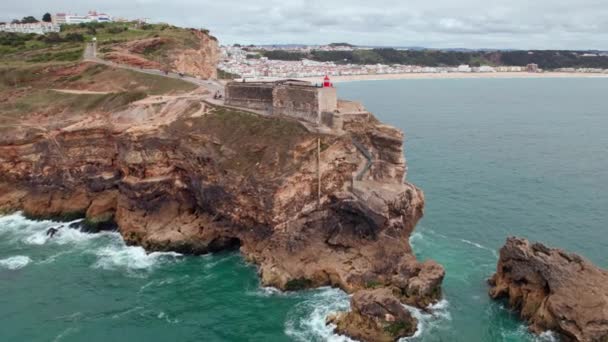 在葡萄牙纳扎尔镇 空中俯瞰着一座坐落在大西洋海岸一个堡垒上的悬崖上的旧灯塔 飞往葡萄牙纳扎尔市的灯塔上空 — 图库视频影像