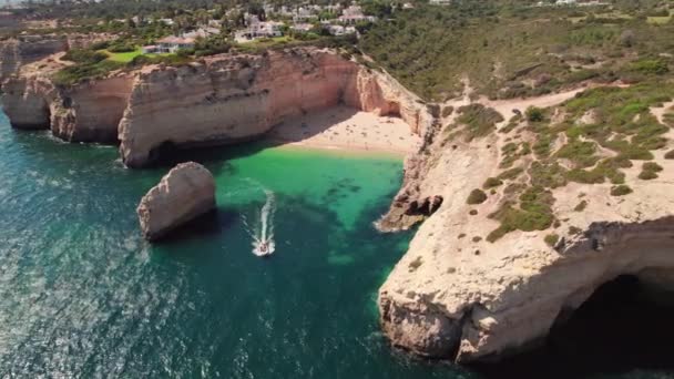 白い砂浜とアルガルヴェ州 南ポルトガルの岩の崖と美しい海の海岸に沿って観光スピードボートに乗る ベナギルビーチの空中ドローン映像 — ストック動画