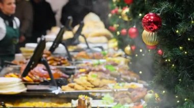 Avrupa 'daki geleneksel Noel pazarının tezgahlarında pişmiş sıcak sokak yemekleri çeşitliliği. Avrupa 'da kışın Noel panayırı. Kamera Noel süslemeleri ile köknar ağacına odaklan.